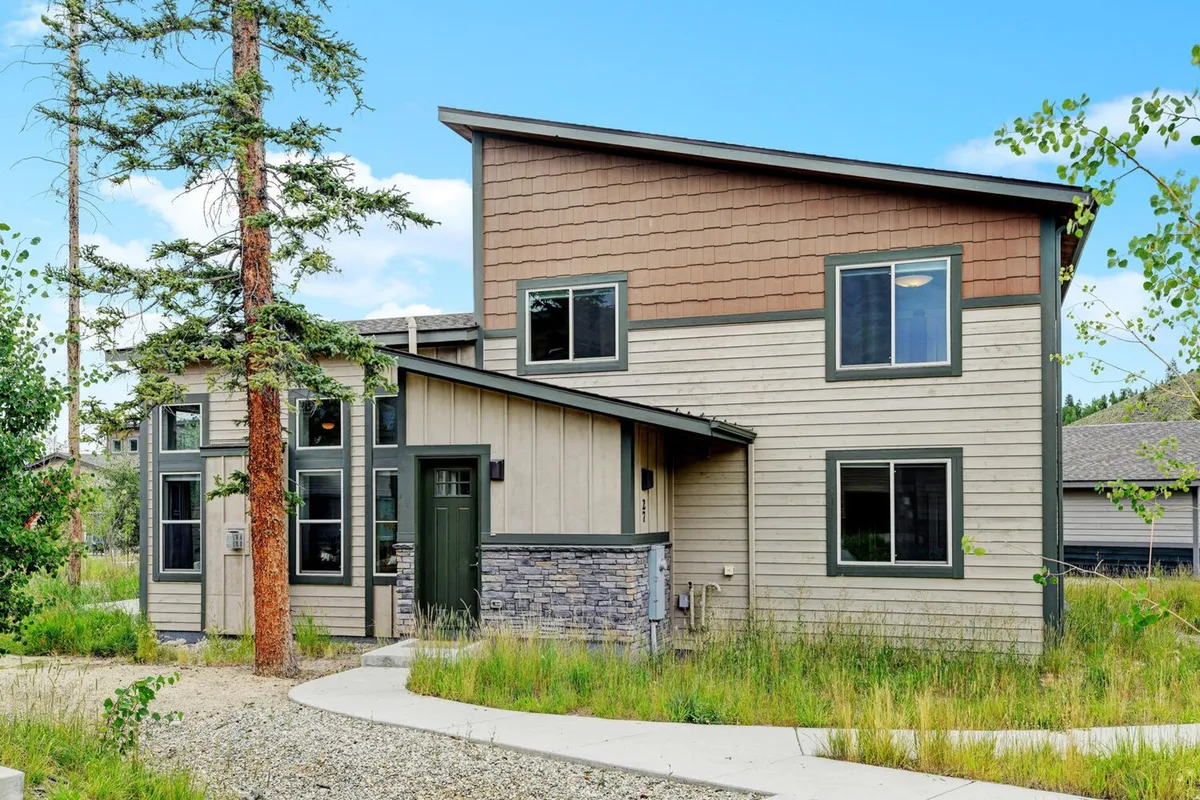 An inviting exterior shot of the home, emphasizing its unique architecture, the bright green front door, and natural landscaping framed by mature trees. The porch and large windows hint at spaces for relaxation and connection with the outdoors, while the tranquil setting invites exploration of the natural surroundings.