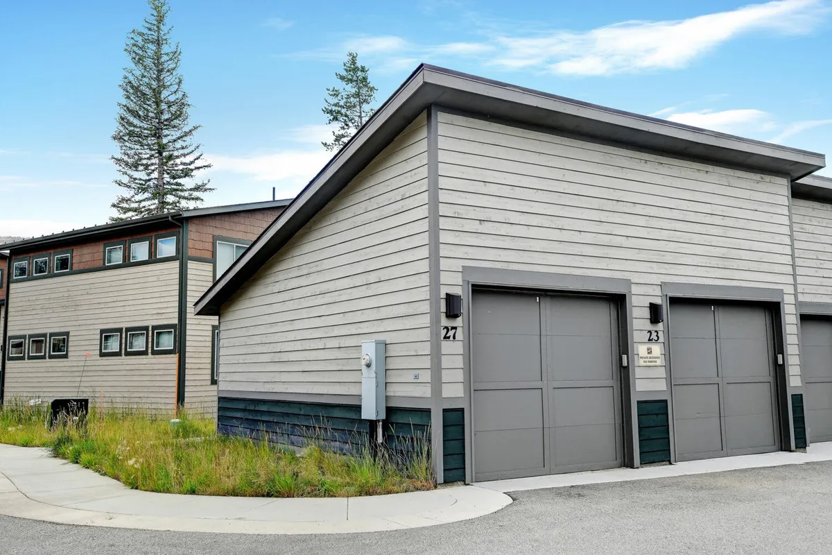 A view of the modern cabin exterior nestled in natural surroundings, with a welcoming driveway and inviting architecture. The setting evokes a sense of mountain seclusion paired with easy access to adventure.