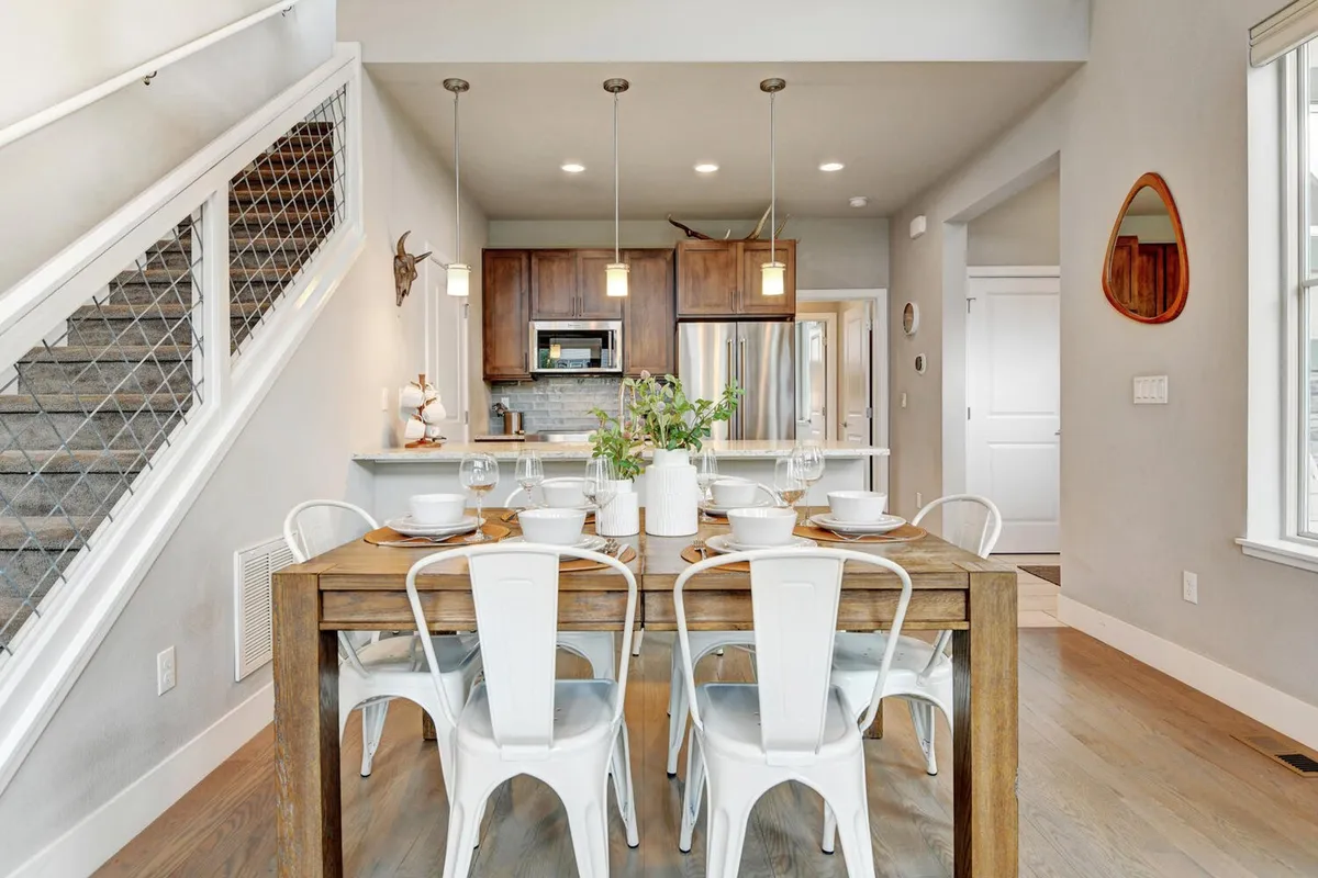 This angle presents the dining area set for a meal, with the kitchen and staircase in the background and pendant lights overhead. The setup is both welcoming and stylish, encouraging memorable group dinners or casual gatherings, and gives a sense of fluid connection between kitchen, dining, and living spaces.