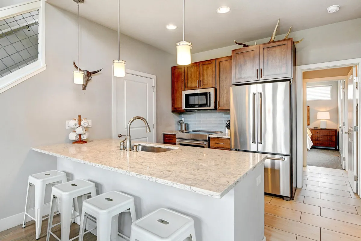 A bright, modern kitchen with a stone countertop island, stainless steel appliances, and comfortable bar stools. The kitchen island is set up for both cooking and casual dining, making it an ideal space for socializing over coffee or preparing hearty meals together.