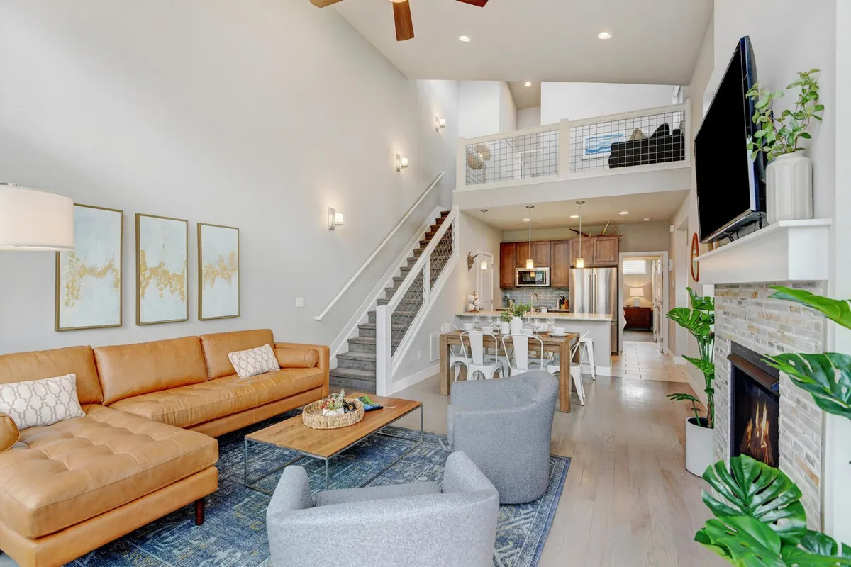 A spacious, open-plan living area featuring a cozy leather sectional sofa, a coffee table, a warm fireplace, and a view into the adjacent kitchen area. The space is set for comfortable family gatherings and relaxing evenings, with tasteful décor and inviting lighting.