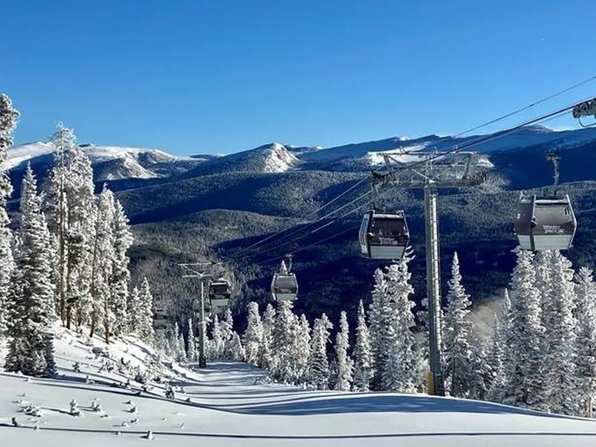 This exterior shot features gondola lifts gliding above snow-covered trees with the dramatic backdrop of a mountain range and a clear blue sky. The scene captures the adventure and natural beauty of the area, inviting guests to experience both action and tranquility.