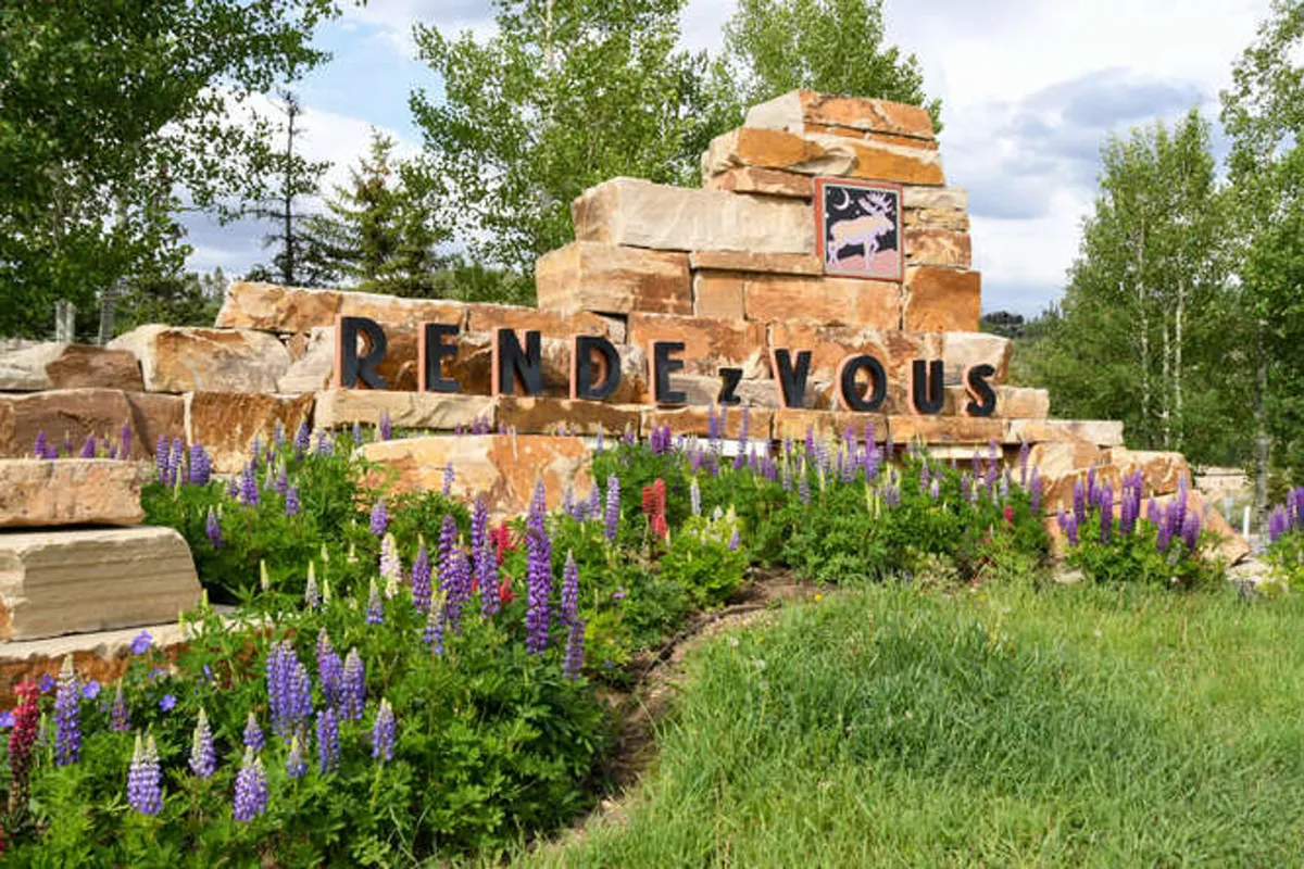 An inviting view of a stone sign framed by colorful seasonal flowers and lush greenery, suggesting a welcoming community and well-kept outdoor spaces.