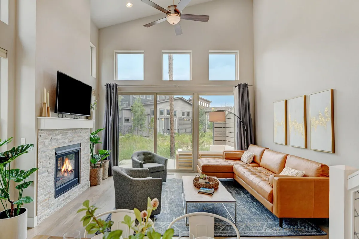 This image captures the heart of the open-concept living area, featuring a cozy fireplace surrounded by plush seating, a large window letting in ample sunlight, and a dining table in the background. The space feels inviting and perfect for family gatherings or relaxing evenings, with a clear line of sight through the shared living and dining zones.