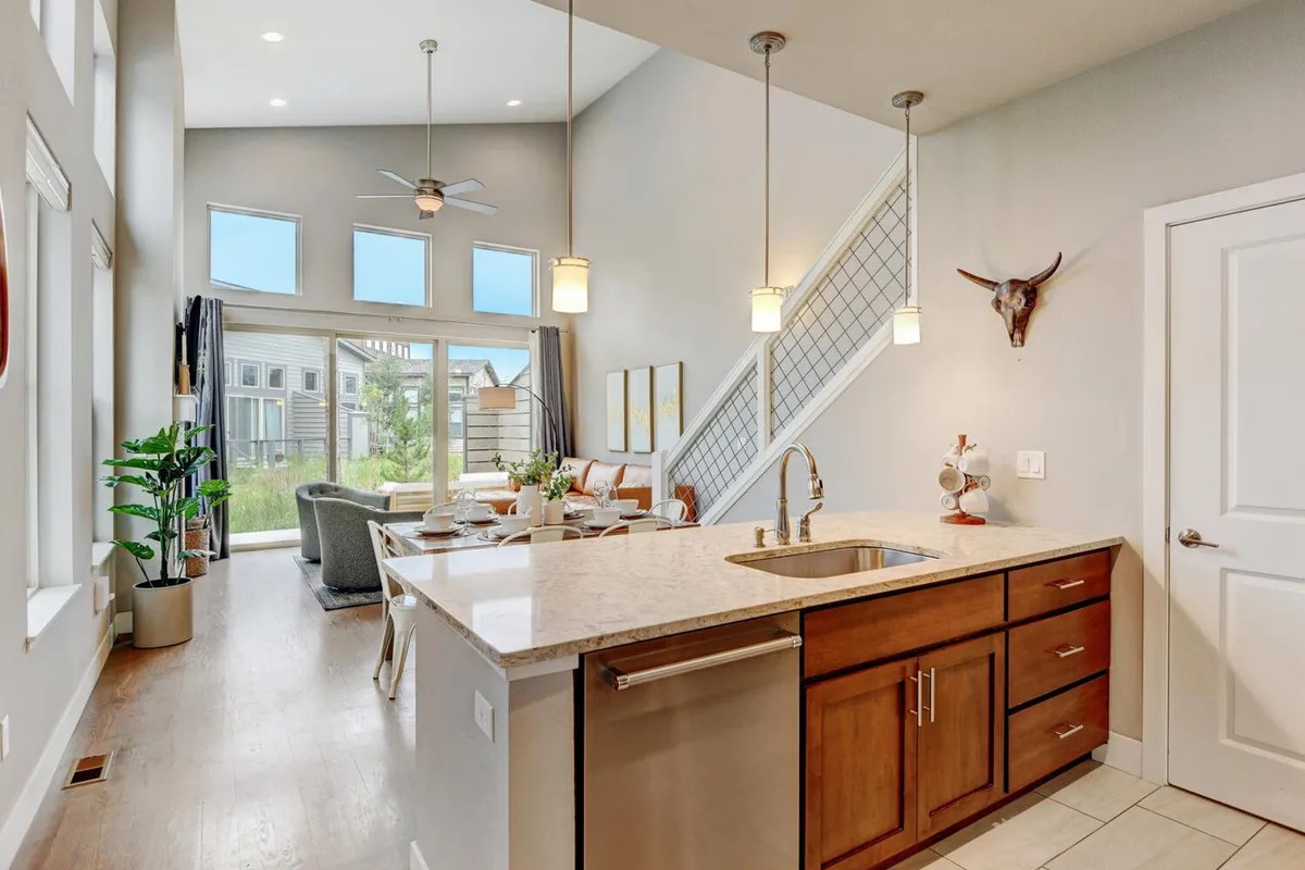 An open-plan interior showcasing a modern kitchen island, large windows with abundant natural light, a staircase, and a comfortable living area with a sofa. The space feels inviting and upscale, suitable for gatherings and relaxation after a day of adventure.