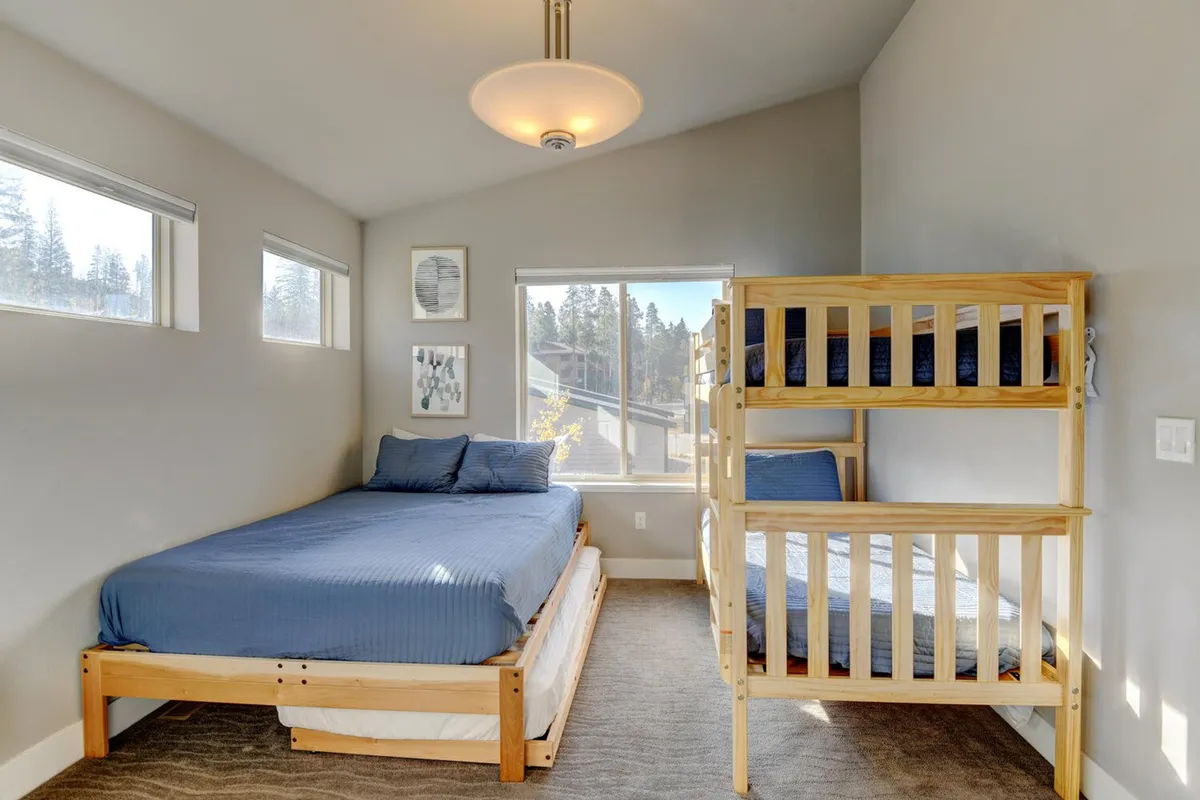 A cozy guest room featuring a queen bed, a twin-over-twin bunk bed, and a large window. The room is bright and welcoming, with playful artwork on the wall, making it ideal for families or groups of friends with flexible sleeping arrangements.