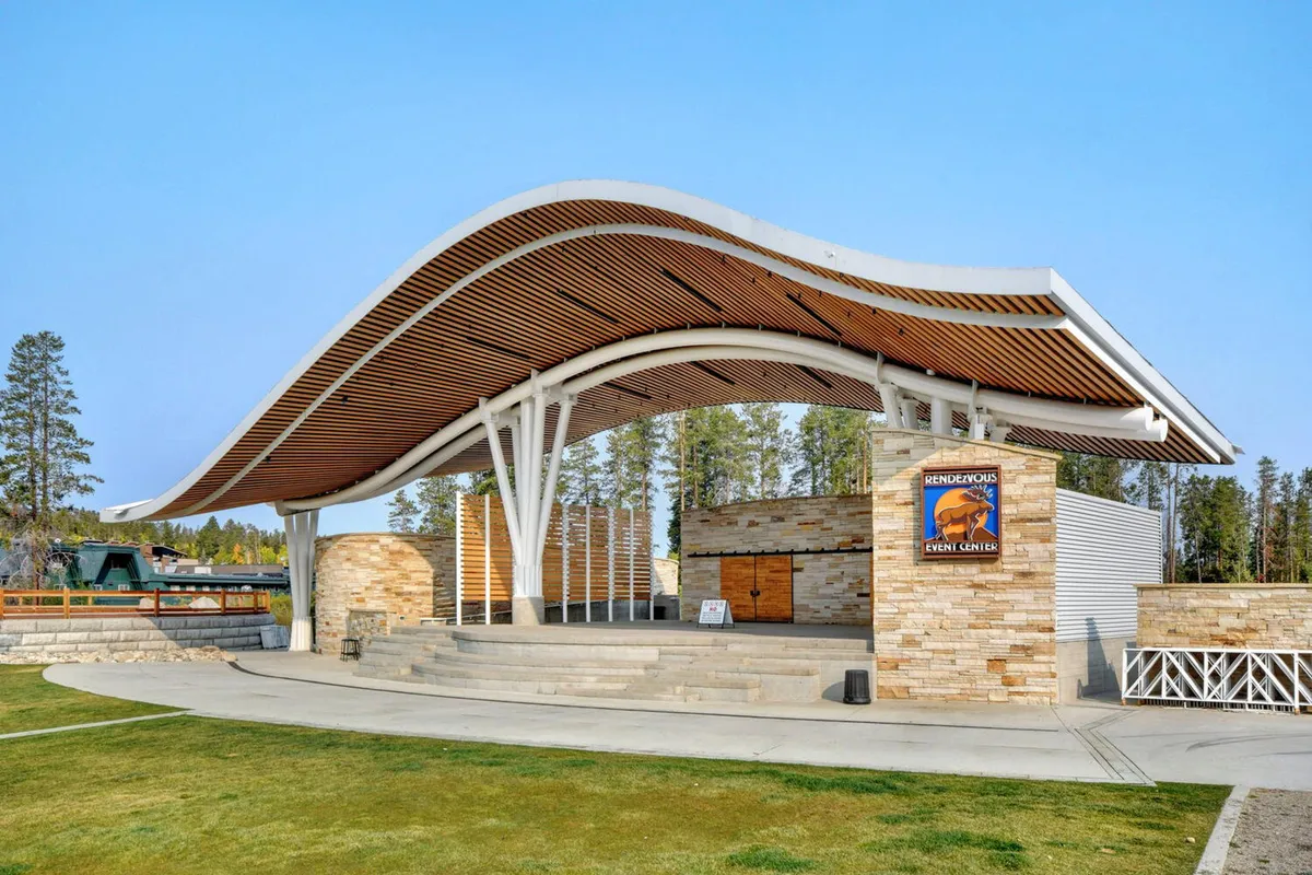 An open-air community stage with a distinctive curved roof and stone walls, set up for outdoor performances and gatherings. The stage is surrounded by open space, hinting at the potential for concerts and local events.